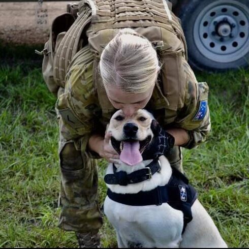 Military woman kissing top of dogs head